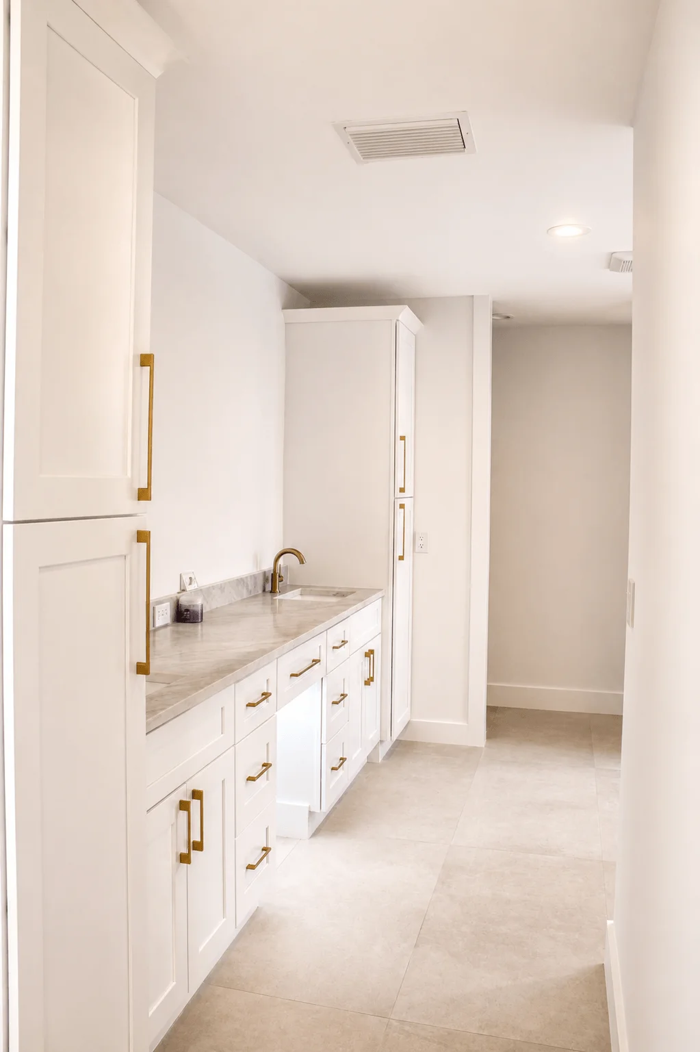 Custom white laundry room with built-in cabinets, marble countertop, and gold hardware
